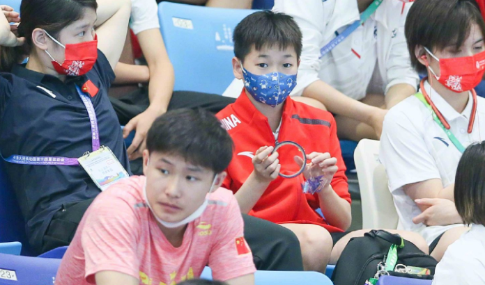 全红婵现身看台！目睹国家队师哥夺冠，戴卡通口罩，专注玩手机